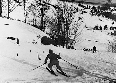 Dieses Foto zeigt 1937 den Hahnenkamm-Slalom am Ganslern. Der Hahnenkamm-Slalom wurde vielfach von den Athleten als „der schwierigste Slalomhang der Welt“ bezeichnet. Grund sind die zahlreichen Übergänge, Wellen, Steilhang, Turn und letztlich der Flachteil vor dem Ziel verlangt von den Sportlern alles ab.